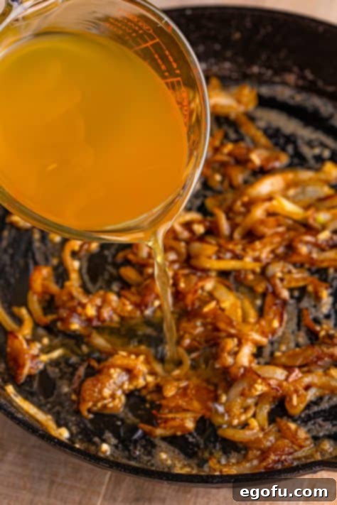 pouring chicken stock into onions in skillet.