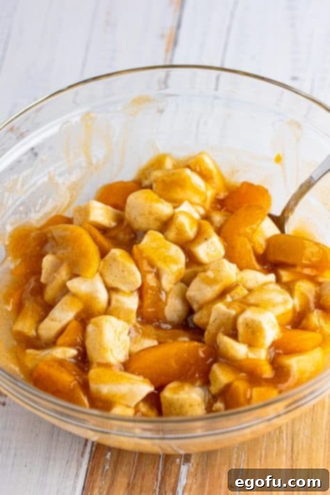 A mixing bowl with biscuit dough pieces, peach pie filling, brown sugar, melted butter, vanilla, and cinnamon.