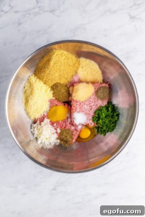 Hand-Rolled Meatballs 5 A mixing bowl with ground beef, ground pork, eggs, pecorino romano cheese, bread crumbs, onion, parsley, parmesan cheese, garlic powder, onion powder, dried oregano, pepper, salt, and basil, ready for mixing.