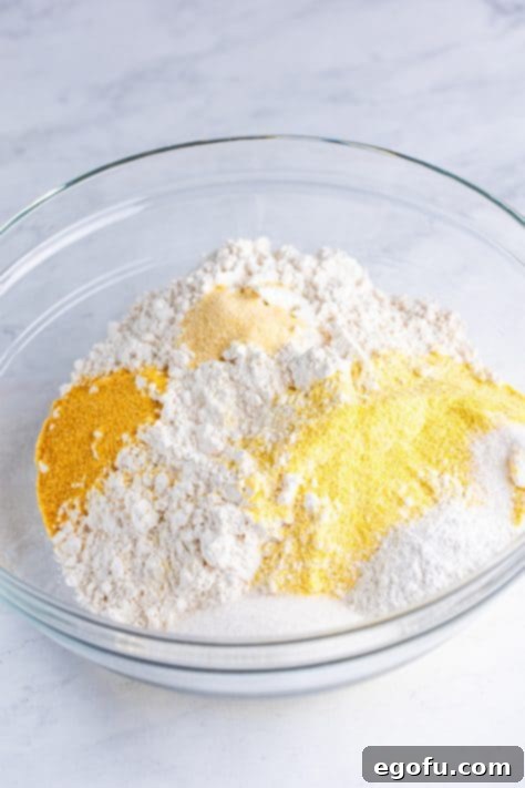 A mixing bowl with yellow cornmeal, flour, sugar, baking powder, garlic powder, onion powder, and salt.