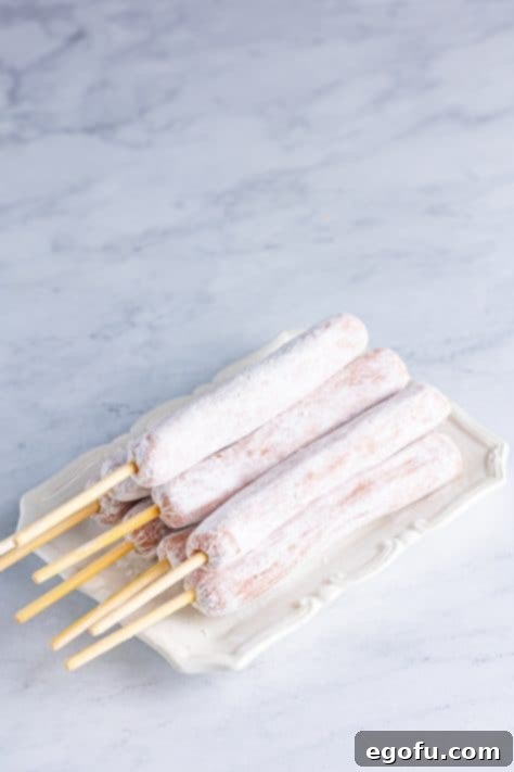 Flour coated hot dogs on skewers on a plate.