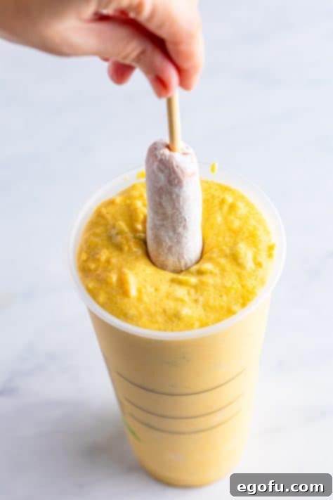 Flour coated hot dogs being dipped in corn dog batter.