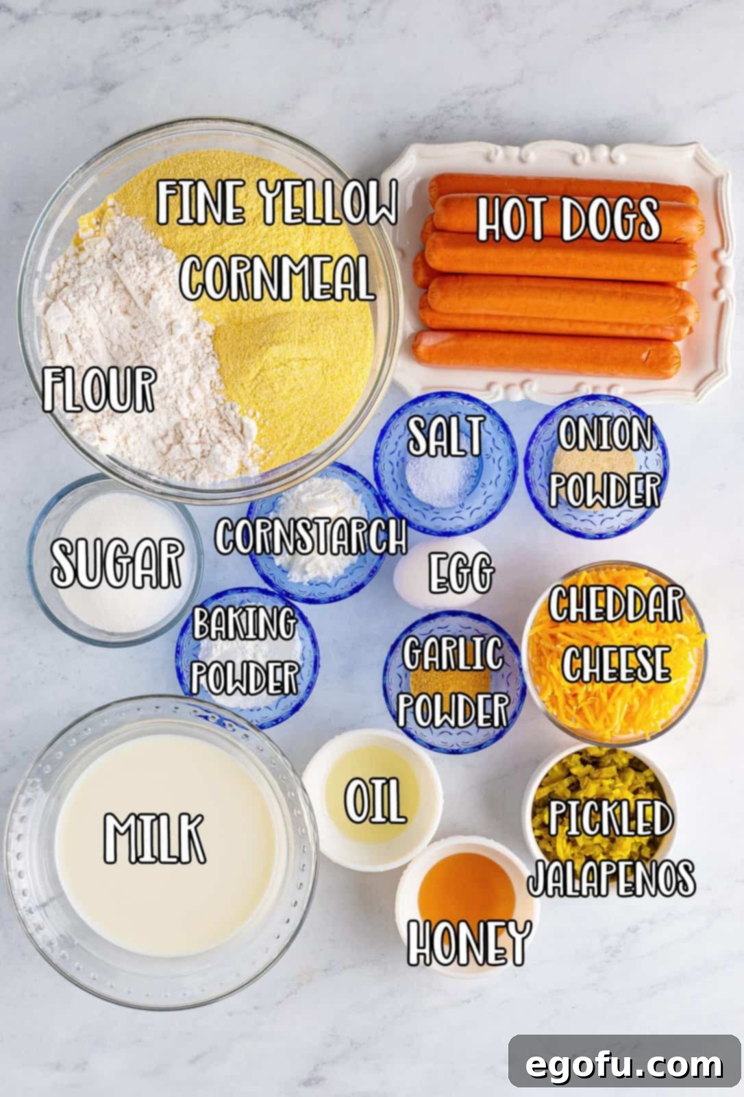 A visual collage of all ingredients needed: yellow cornmeal, flour, sugar, baking powder, garlic powder, onion powder, salt, whole milk, egg, vegetable oil, honey, shredded cheddar cheese, pickled jalapenos, and hot dogs.