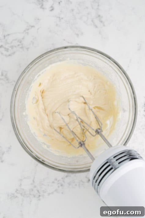 A mixing bowl with softened cream cheese, powdered sugar, caramel sauce and vanilla extract.