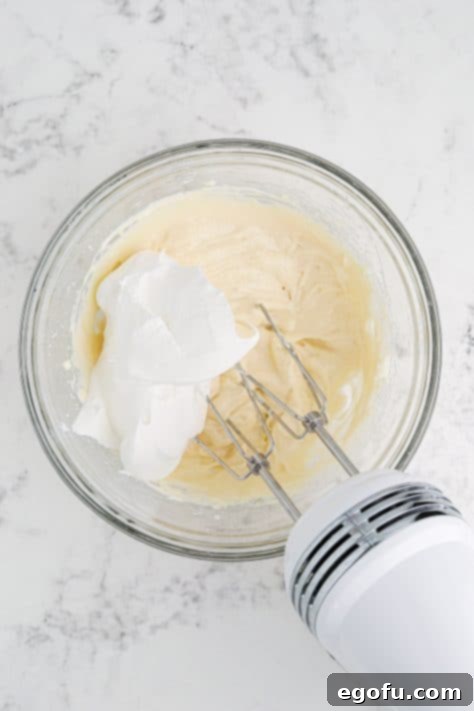 Whipped topping added to softened cream cheese, powdered sugar, caramel sauce and vanilla extract in a mixing bowl.
