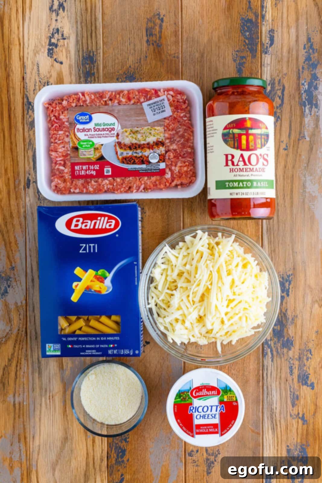 Ziti pasta noodles, Italian ground sausage, pasta sauce, Grated Parmesan cheese, ricotta cheese, and shredded mozzarella cheese laid out as ingredients.