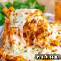 A close up of a large serving of Baked Ziti being taken from a casserole dish.