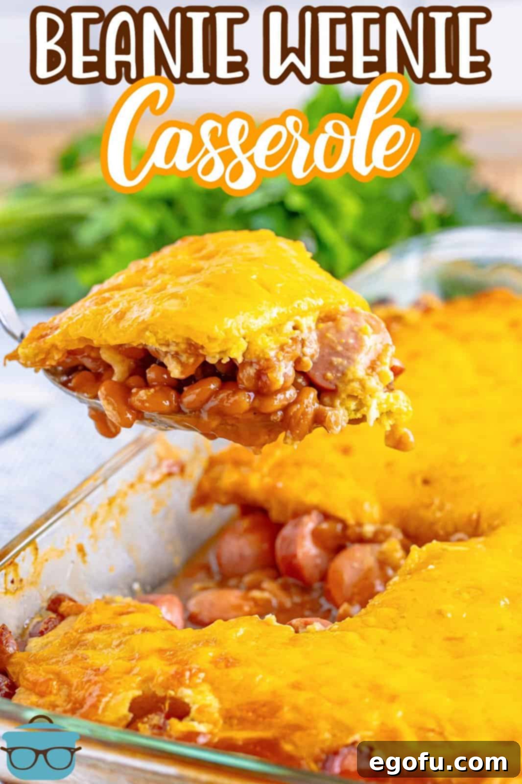 A serving utensil holding a generous portion of Beanie Weenie Casserole over a baking dish of the freshly baked meal.