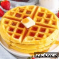 Looking down on a small stack of golden Buttermilk Waffles with a pad of butter melting on top and rich maple syrup drizzled over them.