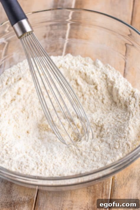 A whisk, flour, baking powder, and sugar in a glass bowl.