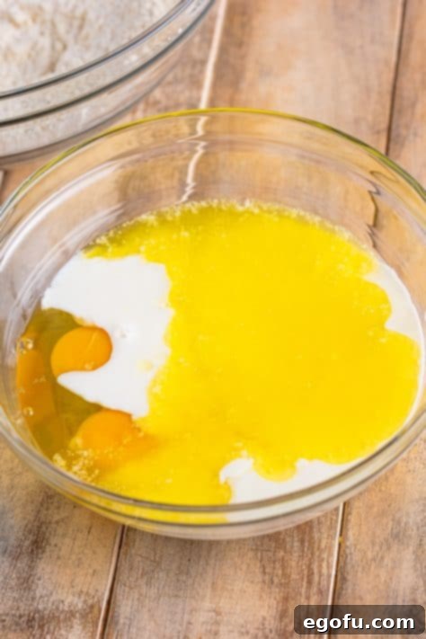 A glass mixing bowl with eggs, buttermilk, melted butter, and vanilla.