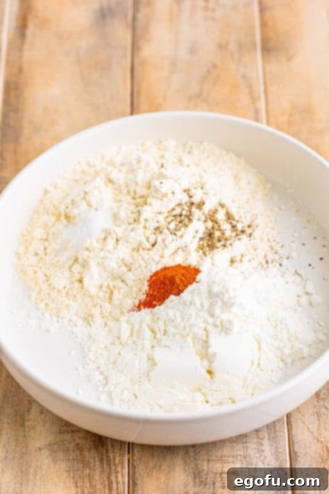 A shallow mixing bowl with flour, cornstarch, salt, paprika, and pepper.