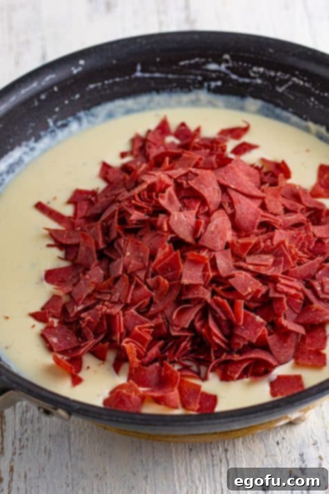 Chopped beef added on top of creamy sauce in a skillet.