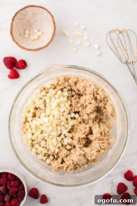 White chocolate chips on top of cookie dough in a bowl.