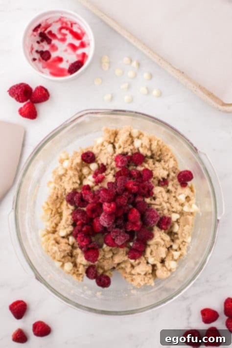 Raspberries on top of cookie dough in a bowl.