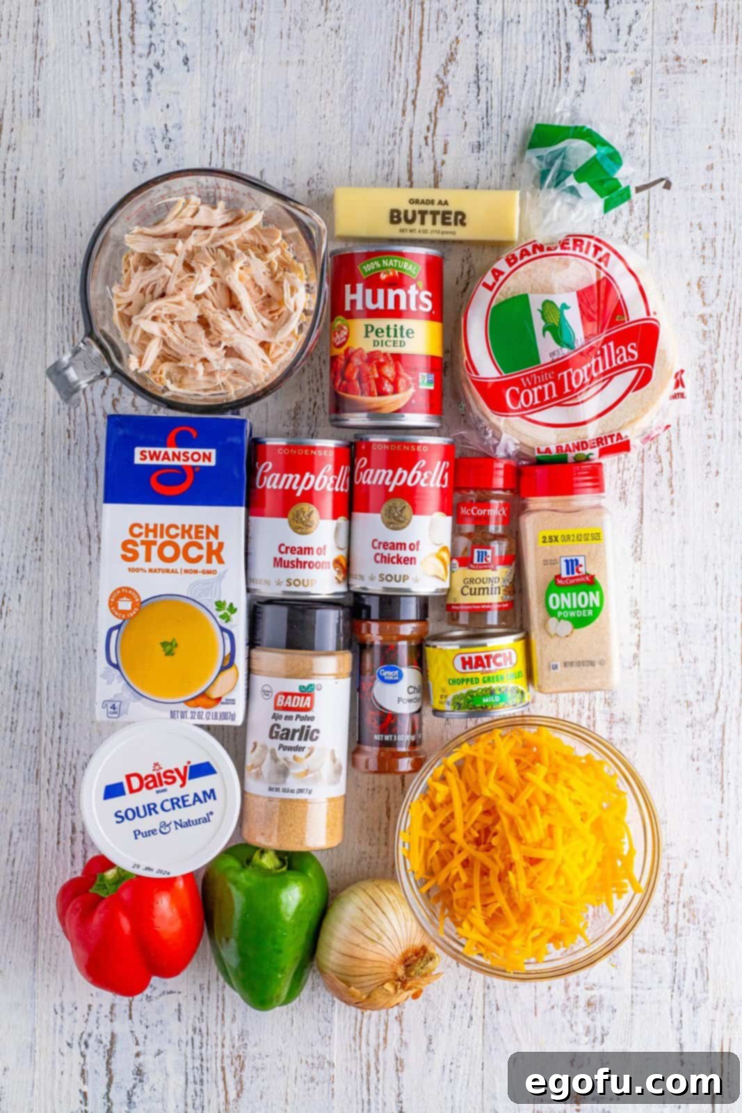 Rotisserie chicken, cream of mushroom soup, cream of chicken soup, petite diced tomatoes, green bell pepper, red bell pepper, cheddar cheese, butter, onion, chopped green chiles, chicken stock, sour cream, chili powder, garlic powder, ground cumin, onion powder, and white corn tortillas.