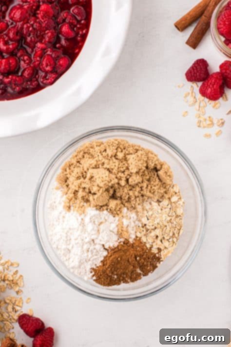 A glass mixing bowl with oats, flour, brown sugar, and pumpkin pie spice.