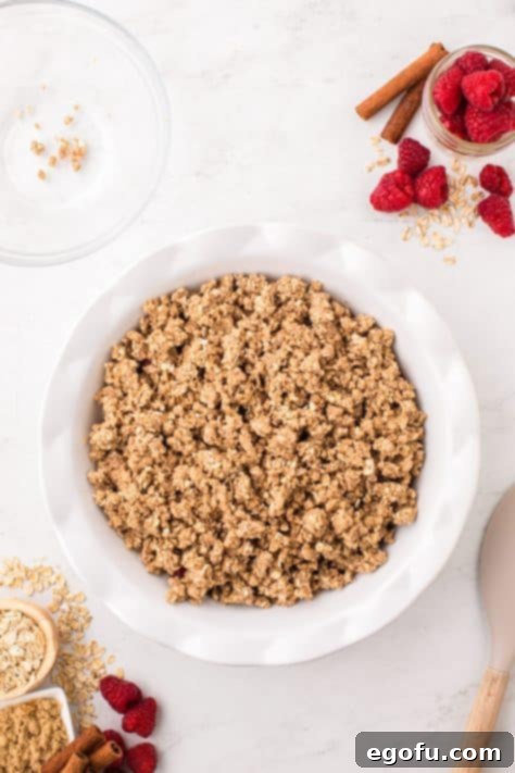 Crumble topping on raspberry filling in a pie plate.