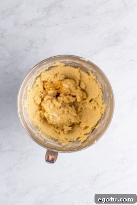 Vanilla extract being added to creamed butter, sugar, and flour in a mixing bowl.