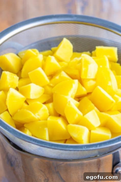 Velvety Stovetop Mashed Potatoes 8 Drained diced potatoes resting in a colander after boiling, with steam gently rising, indicating proper moisture removal.