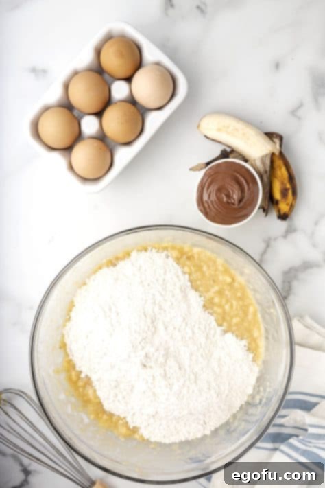 The flour mixture being carefully added to the wet ingredients in a glass mixing bowl, ready for gentle combining.