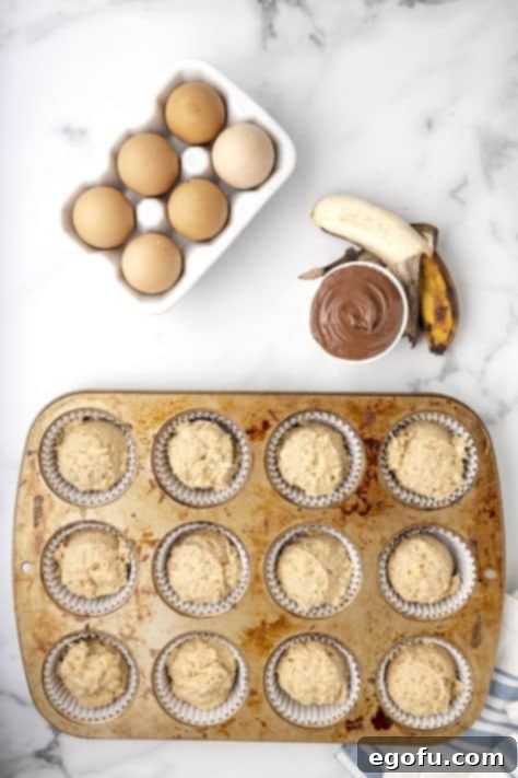 A muffin tin with cupcake liners, each filled three-quarters full with the prepared banana muffin batter.