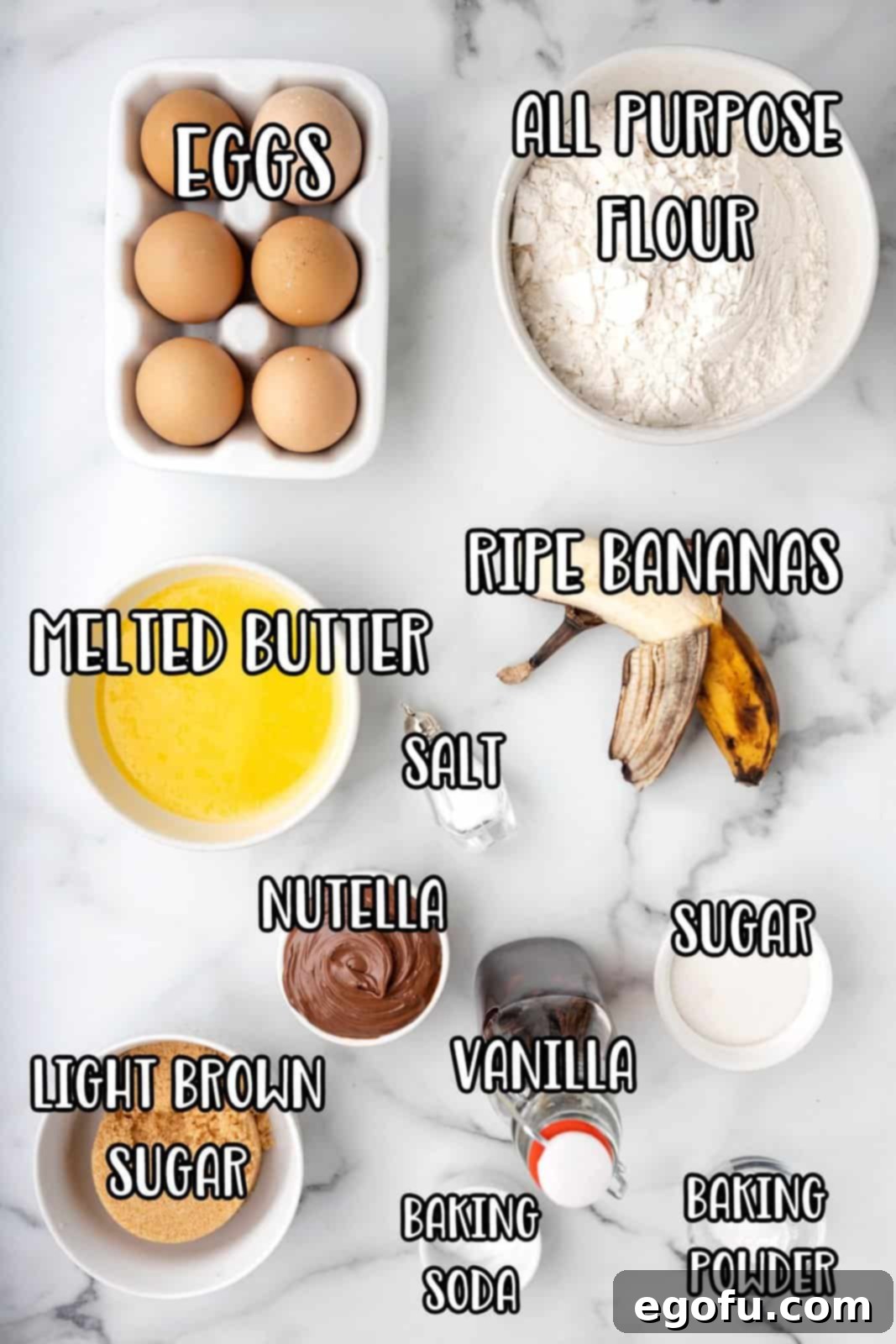 A beautifully arranged flat lay photograph displaying all the fresh and dry ingredients for Nutella Swirl Banana Muffins: eggs, all-purpose flour, melted butter, salt, a jar of Nutella, light brown sugar, ripe bananas, vanilla extract, baking soda, baking powder, and granulated sugar.