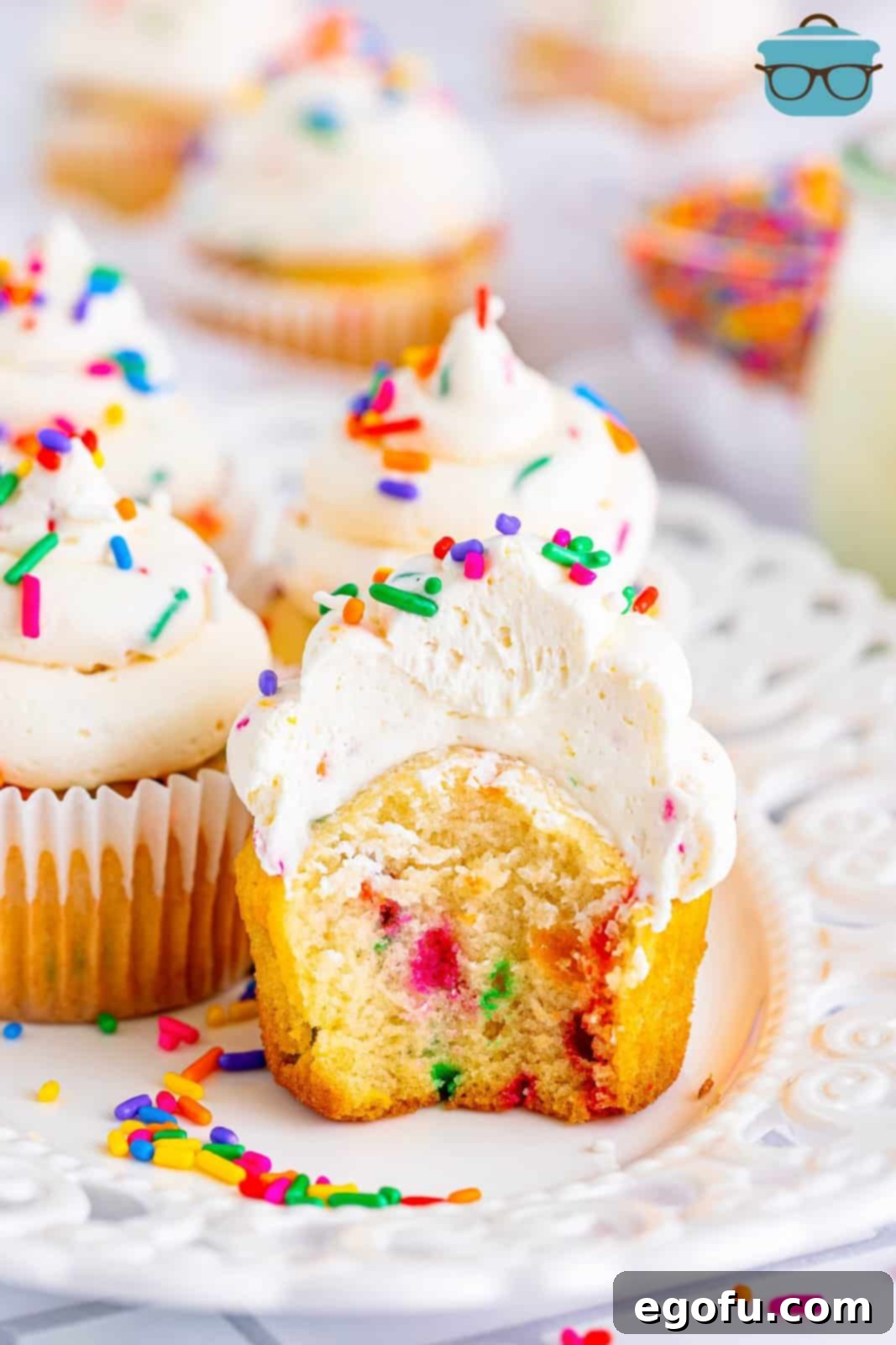 Festive Confetti Cupcakes 2 A small plate with a few Funfetti Cupcakes, one with a bite missing, showcasing its colorful interior and fluffy frosting.