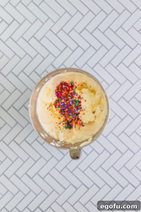 Festive Confetti Cupcakes 22 A pile of vibrant sprinkles being added to a mixing bowl filled with homemade vanilla frosting, ready to be folded in.