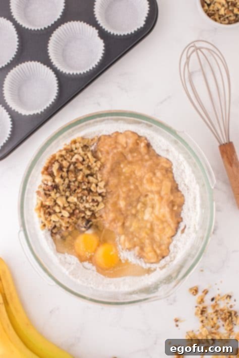 A bowl with cake mix, flour, baking powder, mashed bananas, eggs, and walnuts.