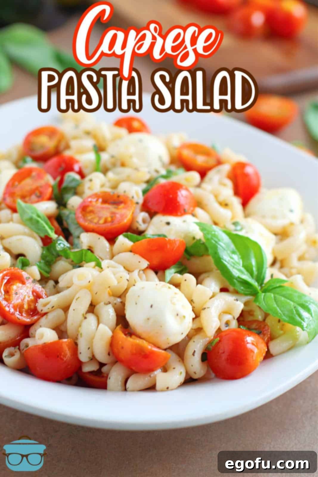 A vibrant white serving bowl generously filled with Caprese Pasta Salad, showing a close-up of the tender pasta, juicy cherry tomatoes, creamy mozzarella pearls, and fresh basil leaves.