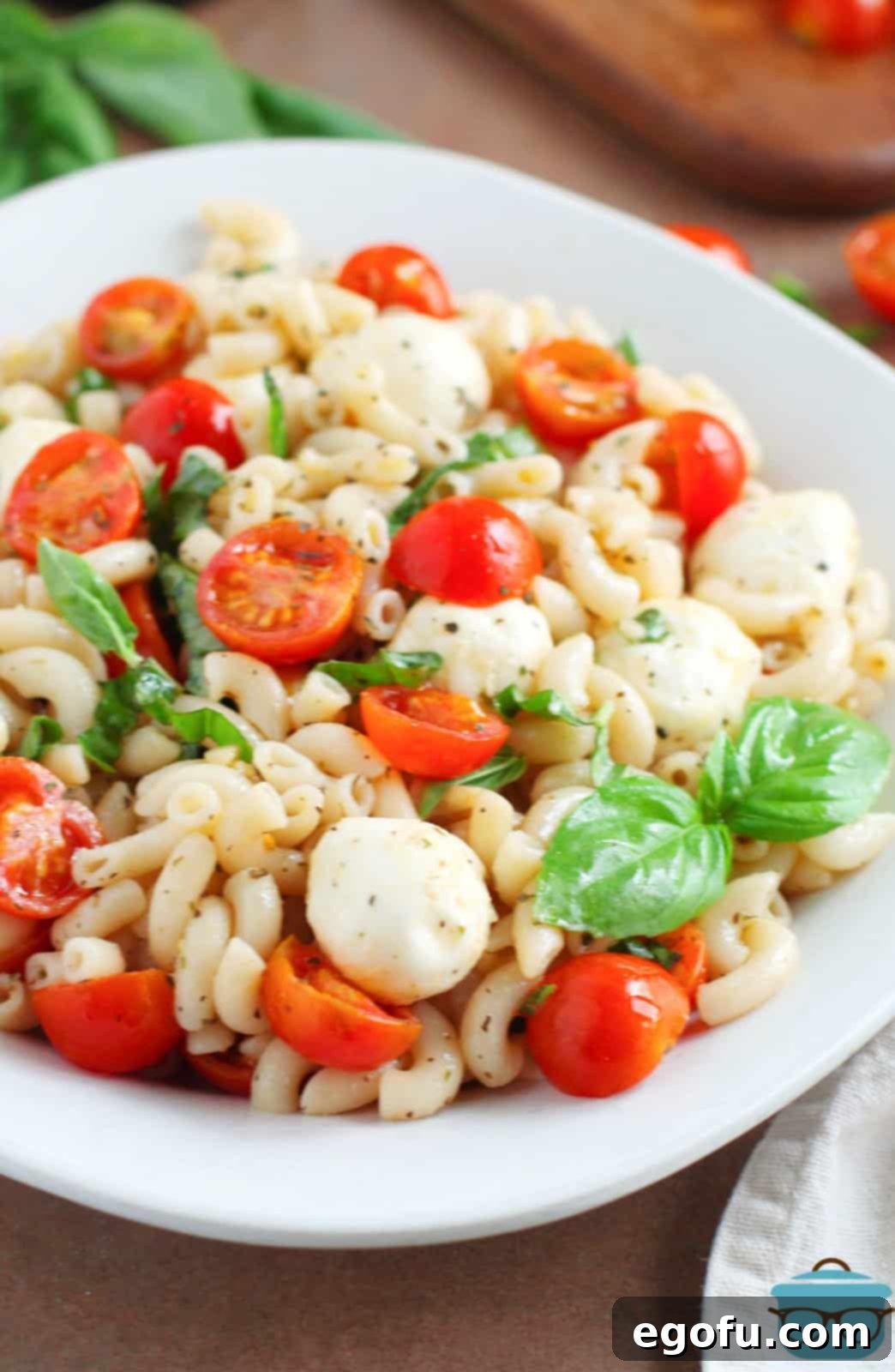 A large Caprese Pasta Salad in a white serving dish, garnished with fresh basil, showcasing its colorful and appetizing appearance.