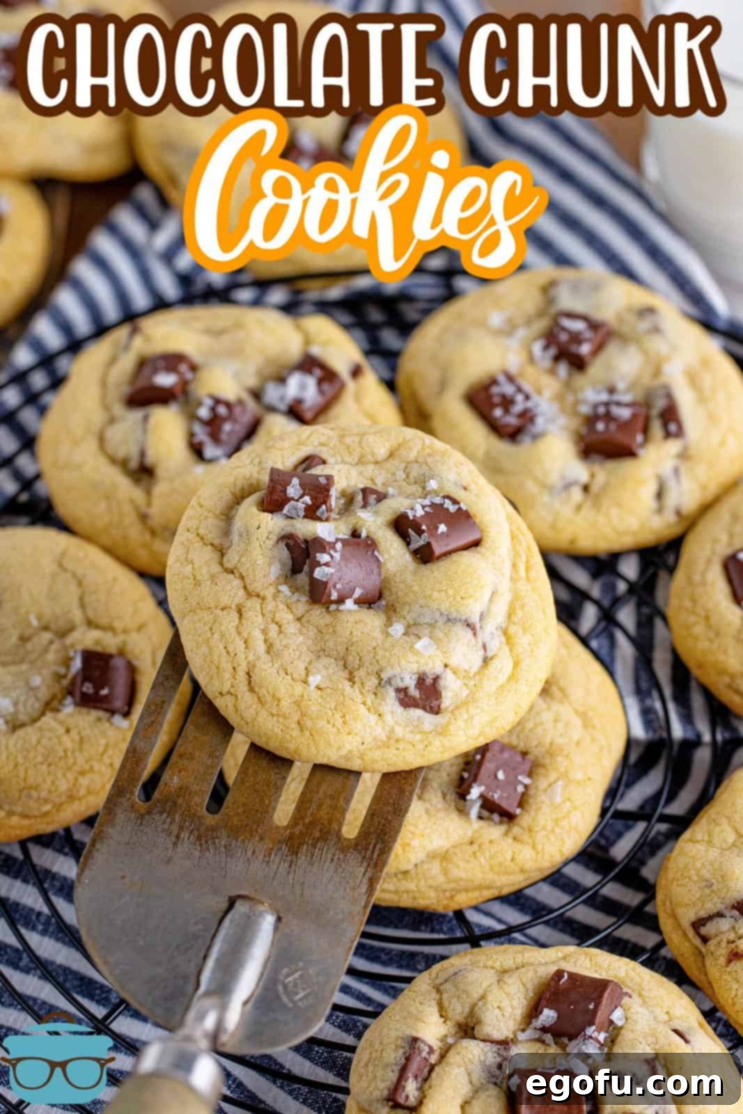 A close-up shot of a golden-brown chocolate chunk cookie being lifted by a spatula from a stack on a wire cooling rack, highlighting its soft interior and melted chocolate chunks, ready for a taste.