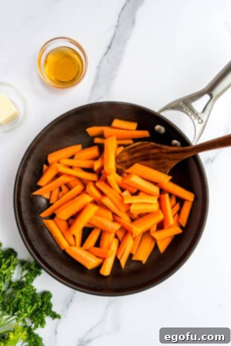 Carrots in a skillet being pushed with a wooden spoon.