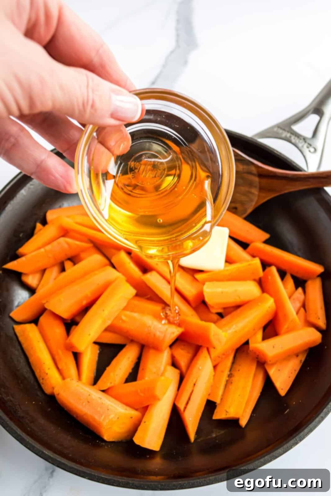 Butter and honey being added to the cooked carrots in a skillet, ready to be stirred into a rich glaze.
