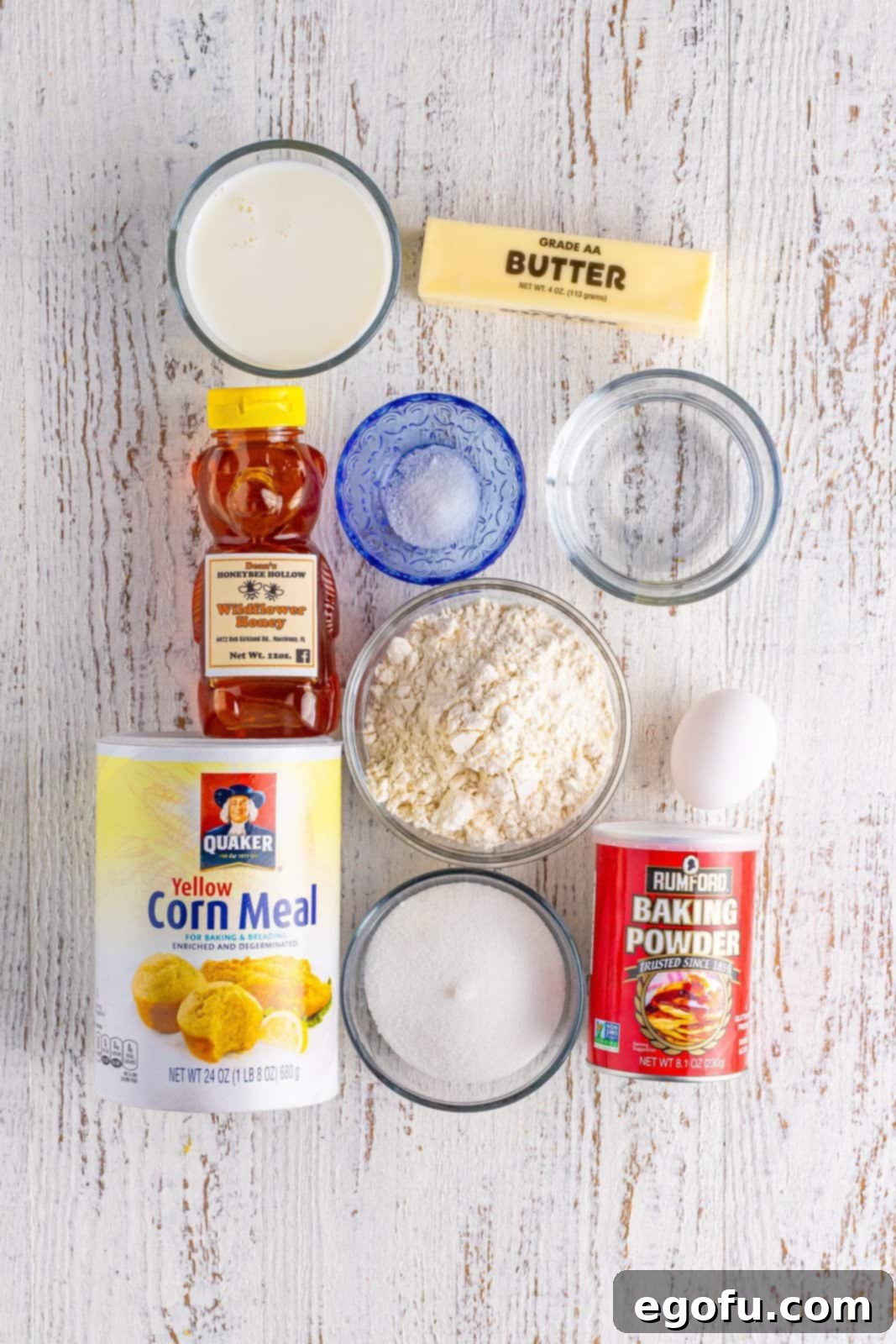 Golden Corn Muffins 4 A vibrant flat lay of all the essential ingredients: yellow cornmeal, egg, butter, all purpose flour, sugar, salt, honey, milk, water, and baking powder.