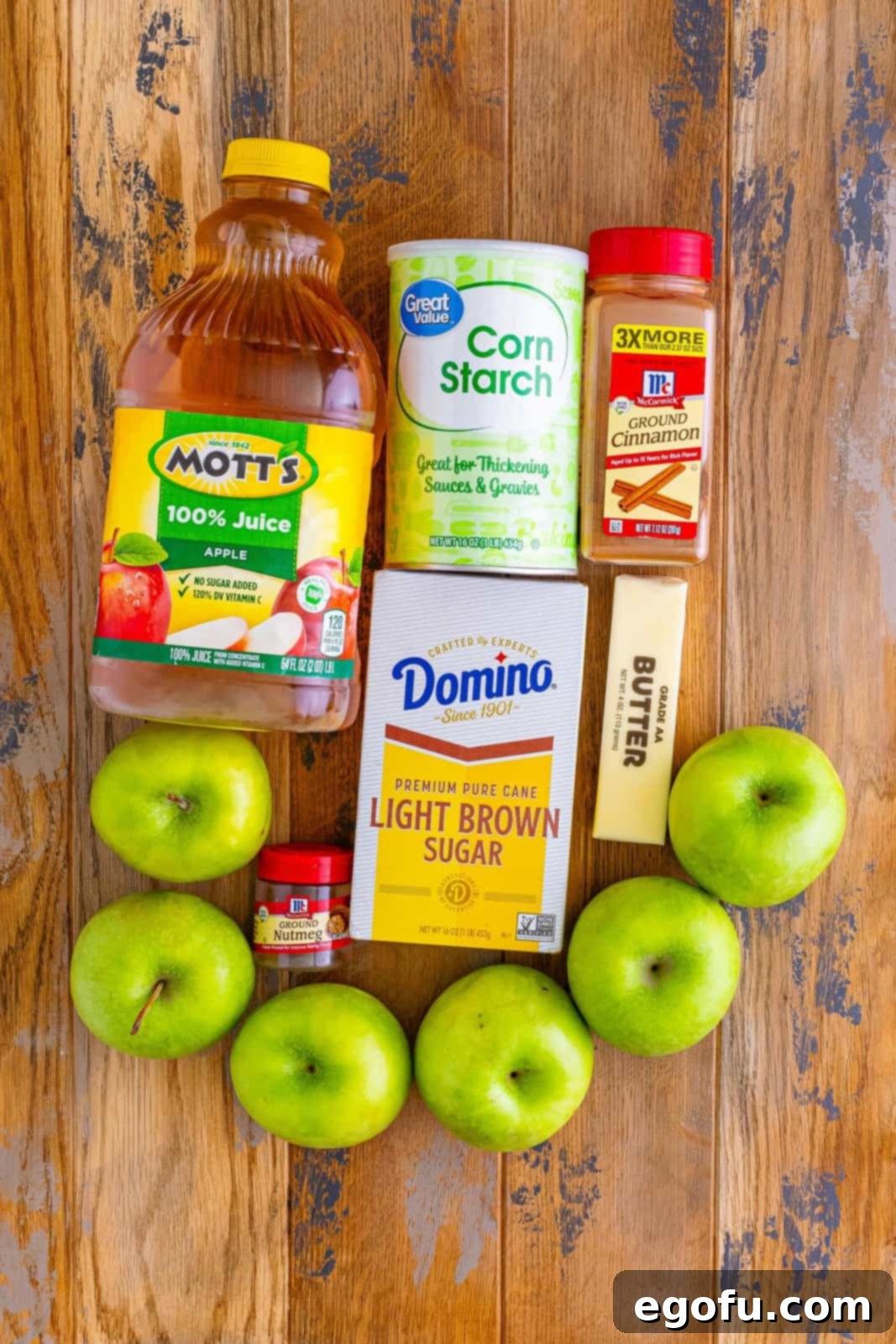 A flat lay photograph of all the ingredients needed for Southern Fried Apples: peeled and sliced Granny Smith apples, light brown sugar, apple juice, a stick of butter, cornstarch, ground cinnamon, and a whole nutmeg.