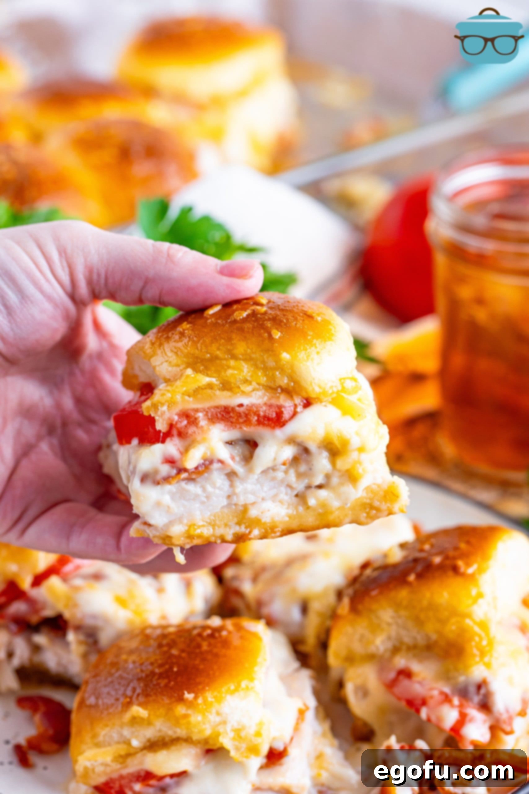 A hand holding a Kentucky Hot Brown Slider above a plate with more of them.