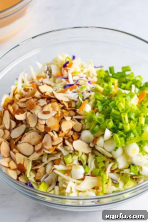 A larger glass mixing bowl with slaw mix, green onions, and almonds.