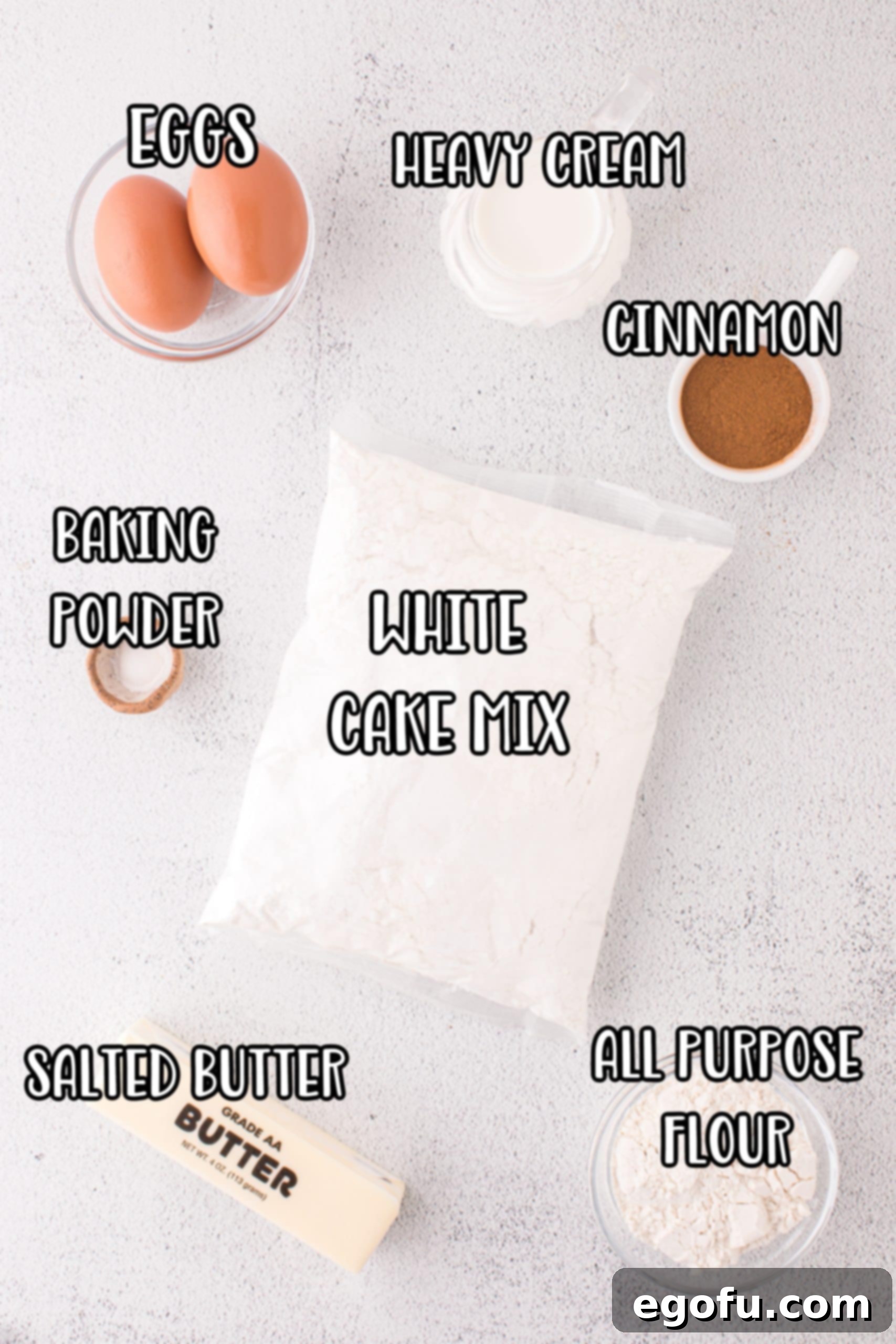 White cake mix, eggs, cinnamon, baking powder, heavy cream, all purpose flour, and butter displayed as ingredients for muffins.
