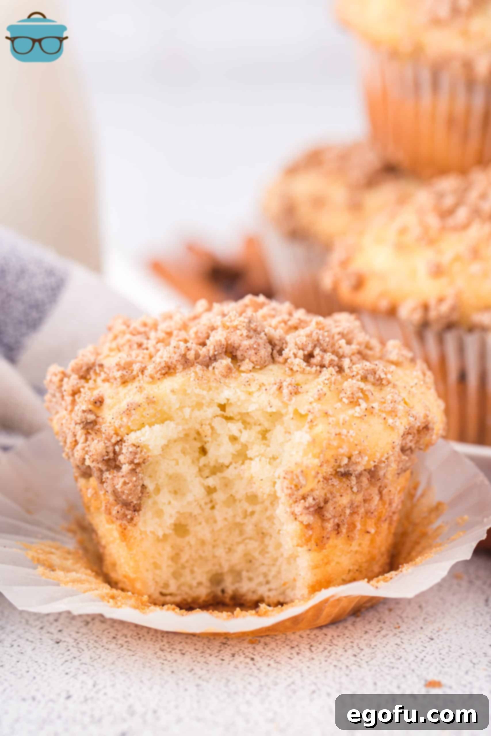 A Cinnamon Streusel Cake Mix Muffin with a bite missing, showing its soft interior and crumb topping.