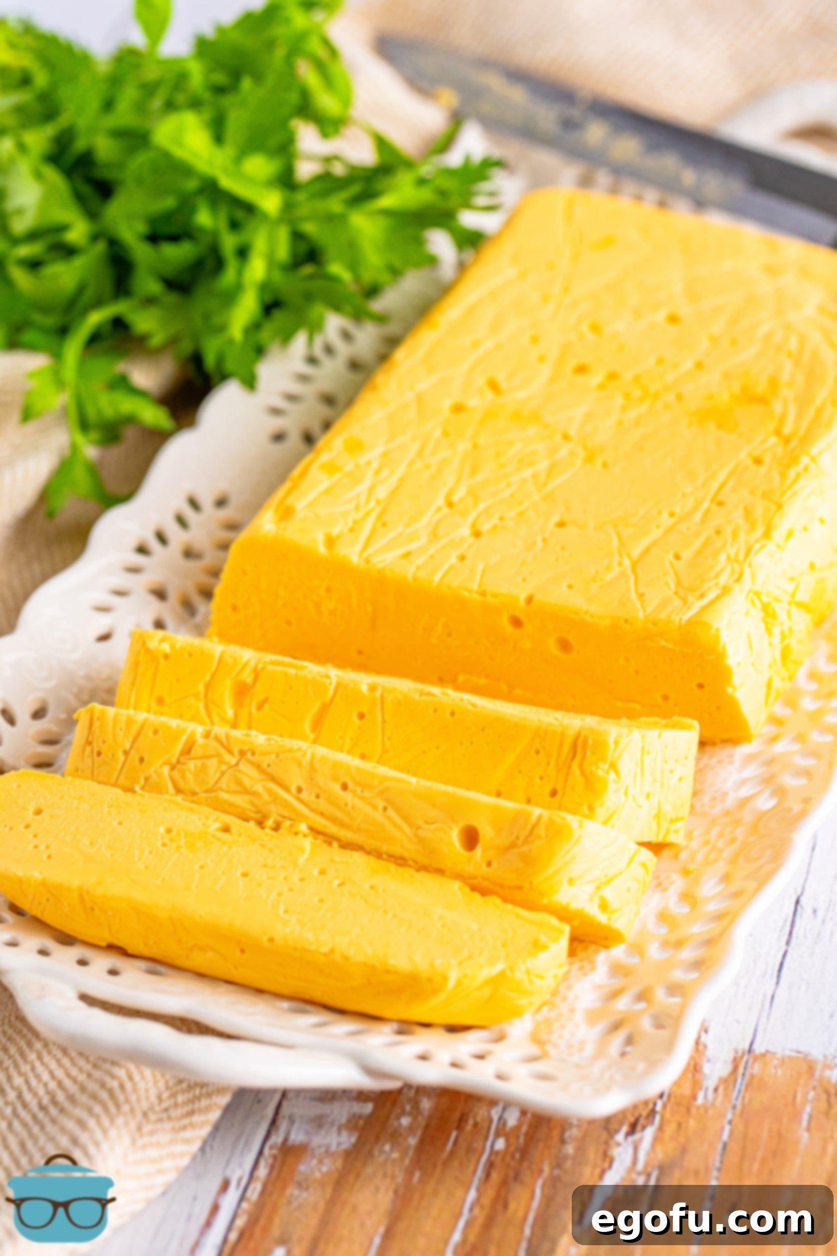 A golden block of creamy Homemade Velveeta cheese, with several smooth slices cut off, resting on a rustic wooden board.