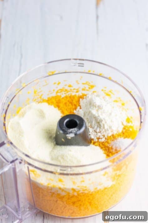 A food processor containing grated cheese, powdered milk, cornstarch, and salt, ready for mixing.