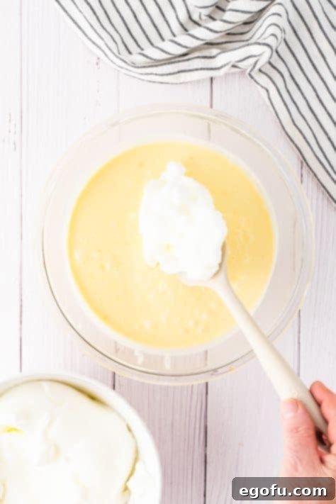 Fluffy egg whites being added to a Lemon Magic Cake batter.