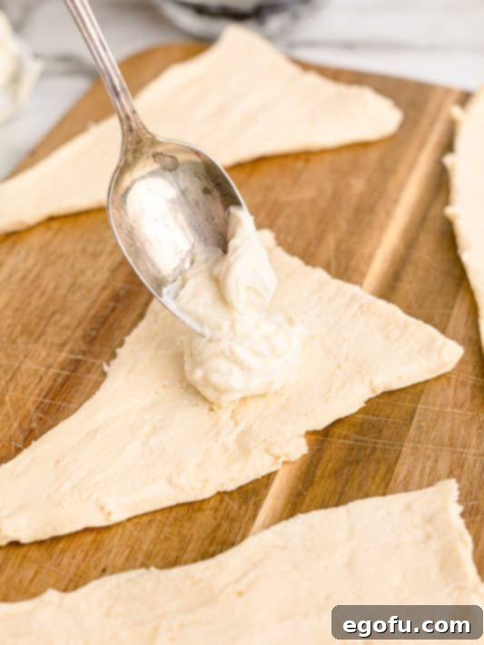 Crescent roll dough rolled out with a spoon putting cheesecake filling on it.