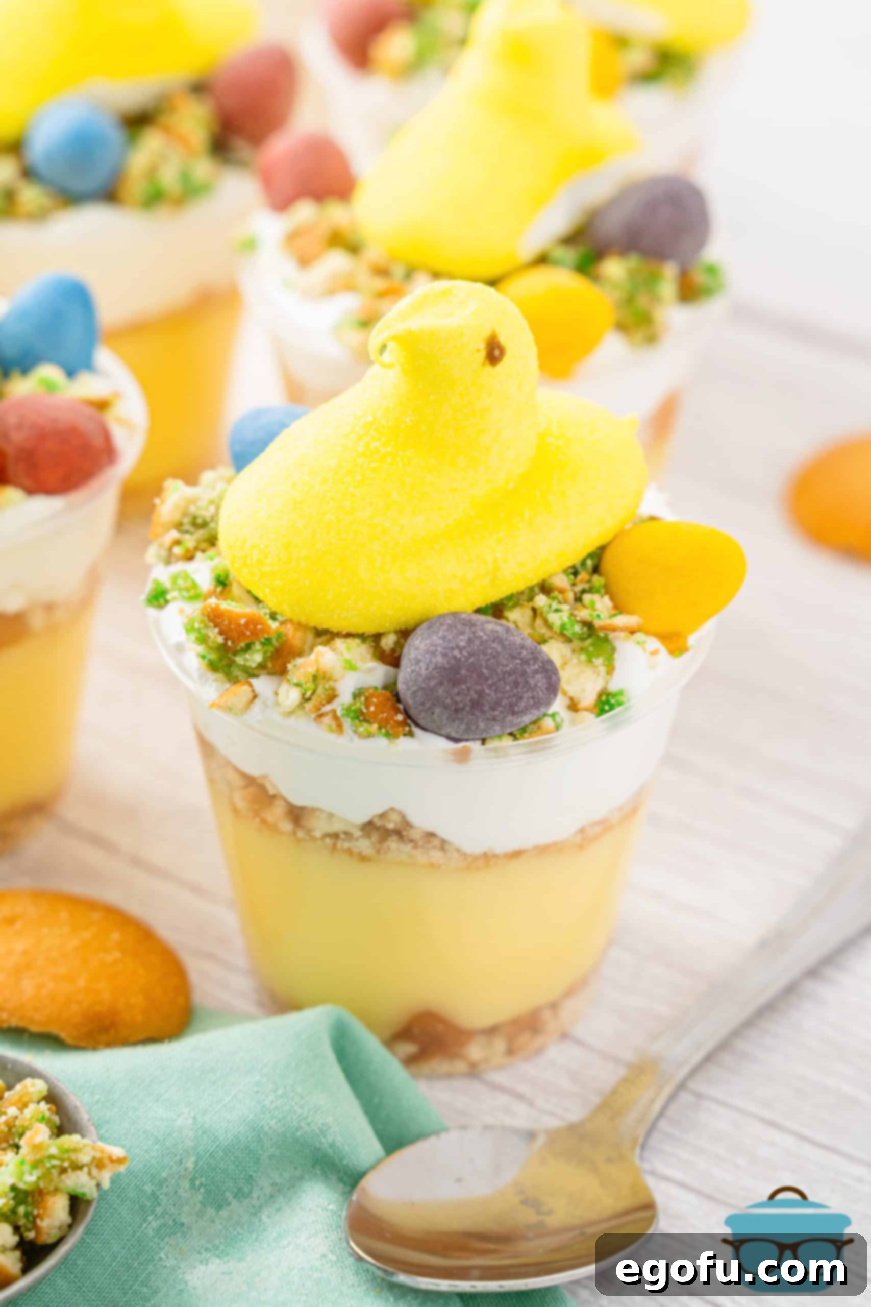 An Easter Banana Pudding Cup with decorative layers, topped with a yellow marshmallow Peep and Cadbury chocolate eggs.