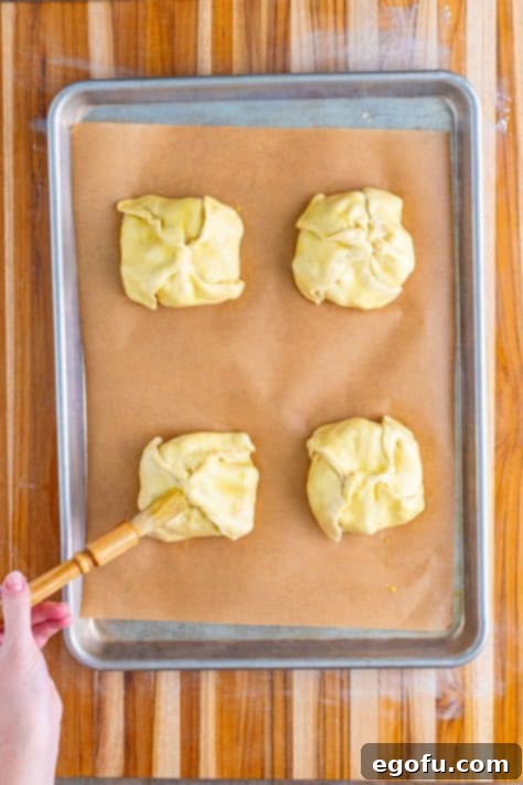 The outside of cream chicken pastries being brushed with an egg wash.
