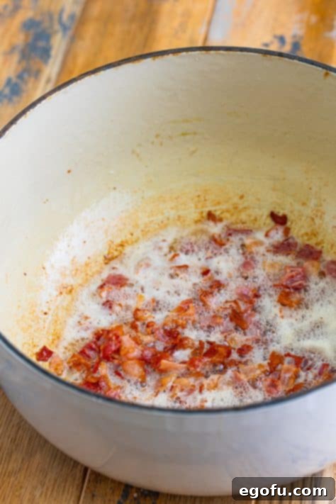 Cooked bacon pieces in a Dutch oven, with rendered grease, ready to be removed.
