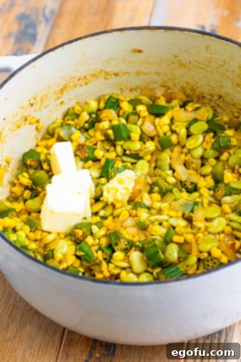 Butter and minced garlic being stirred into the succotash mixture in a Dutch oven.