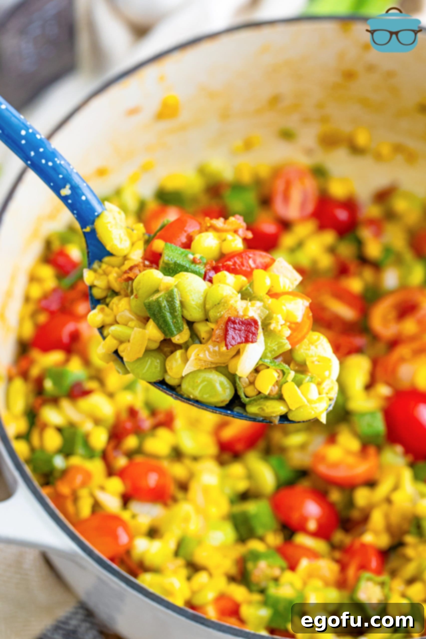A serving spoon lifting a portion of freshly prepared Succotash from a bowl, highlighting its textures and vibrant colors of corn, lima beans, and tomatoes.